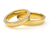 Zwei goldene Hochzeitsringe mit Diamantbesatz liegen übereinander