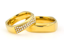 Zwei goldene Hochzeitsringe mit Diamantbesatz und eckiger Form liegen übereinander